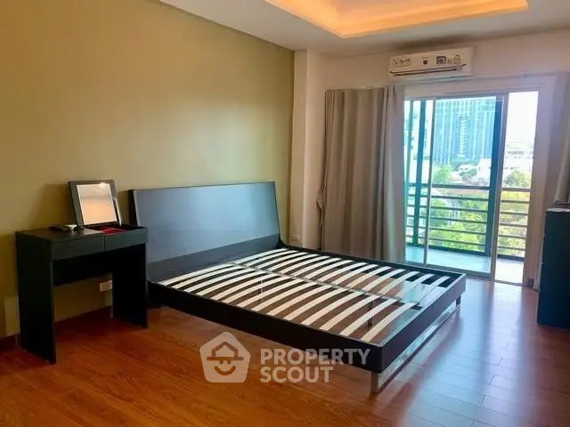 Spacious bedroom with balcony and modern wooden flooring in urban apartment.