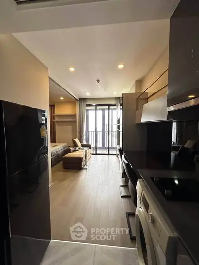 Modern studio apartment with open layout, featuring sleek kitchen and cozy living area leading to a balcony.