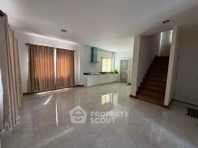 Spacious open-plan living area with modern kitchen and staircase, featuring large windows and elegant curtains.