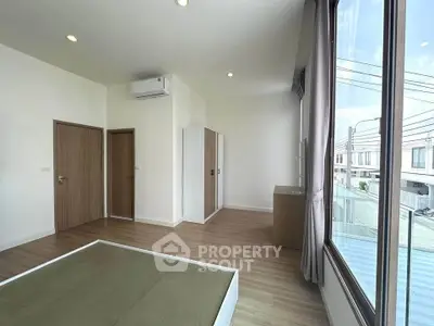 Spacious modern bedroom with large window and wooden flooring in a contemporary home.