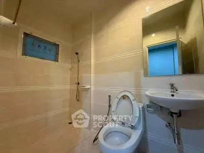 Modern bathroom with sleek fixtures and neutral tiles, featuring a shower and toilet.