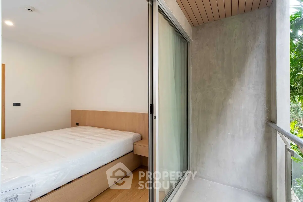 Modern bedroom with sliding glass door to small balcony, featuring minimalist design and natural light.