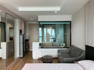 Modern studio apartment with glass partition, cozy sofa, and compact kitchen area.