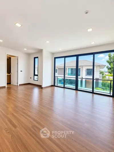 Spacious modern living room with large windows and wooden flooring, offering a bright and airy ambiance.