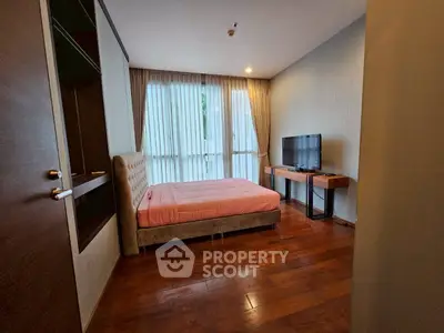 Spacious bedroom with wooden flooring and large window for natural light.