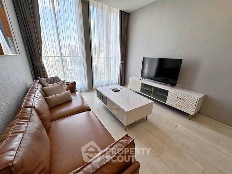 Modern living room with large windows, stylish furniture, and a flat-screen TV, offering a bright and inviting atmosphere.