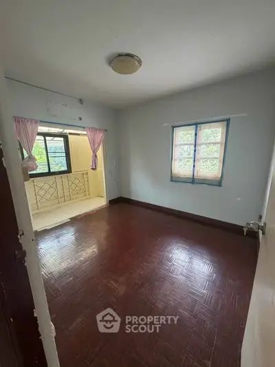 Spacious empty room with wooden flooring and large windows for natural light.