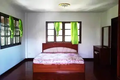 Spacious bedroom with wooden flooring and large windows for natural light.