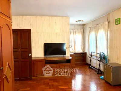 Spacious living room with wooden flooring and natural light, featuring a TV and elegant wooden furniture.