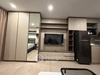 Modern living room with sleek built-in storage and flat-screen TV, adjacent to a stylish kitchen area.