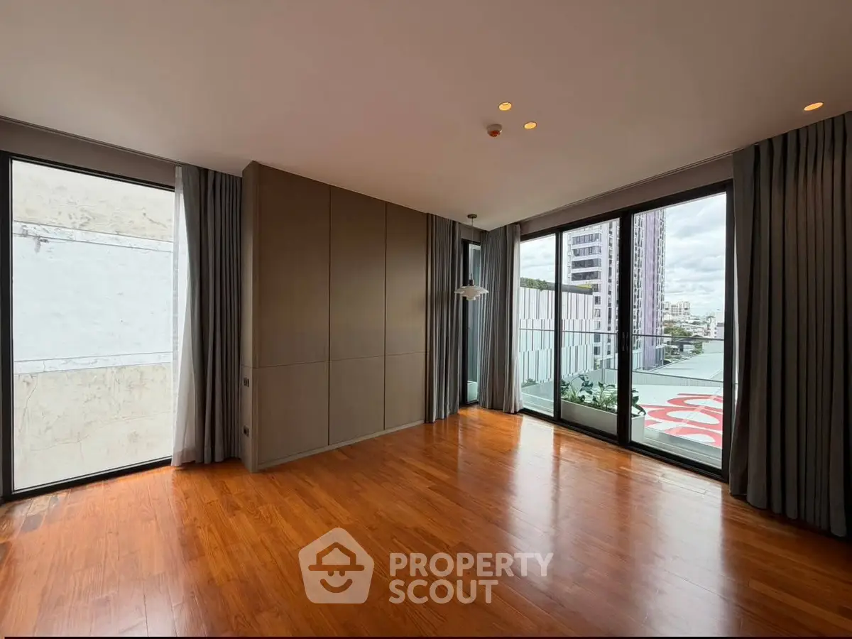 Spacious modern living room with floor-to-ceiling windows and wooden flooring in urban apartment.
