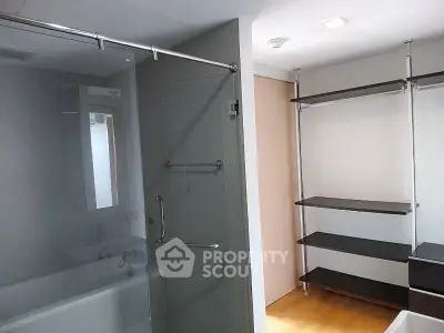 Modern bathroom with glass shower and open shelving unit.