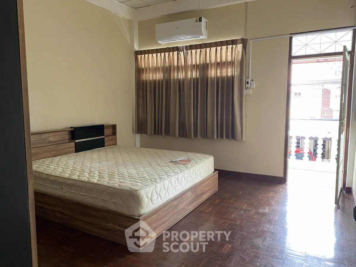 Spacious bedroom with wooden flooring and balcony access in a modern apartment.