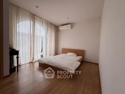 Spacious minimalist bedroom with wooden flooring and large window drapes.