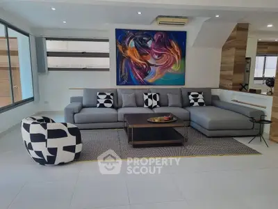 Modern living room with stylish gray sectional sofa and abstract art, featuring large windows and chic decor.