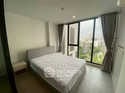 Modern bedroom with large windows offering city views, featuring a comfortable bed and stylish decor.