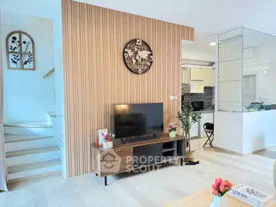 Modern living room with stylish wooden paneling and TV unit, open kitchen view, and elegant decor.