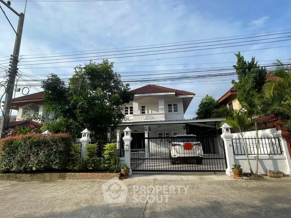 Charming two-story house with gated driveway and lush greenery in a serene neighborhood.