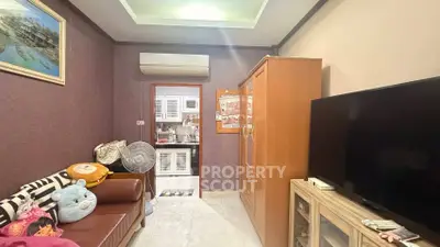 Cozy living room with modern decor and large TV, leading to a compact kitchen.