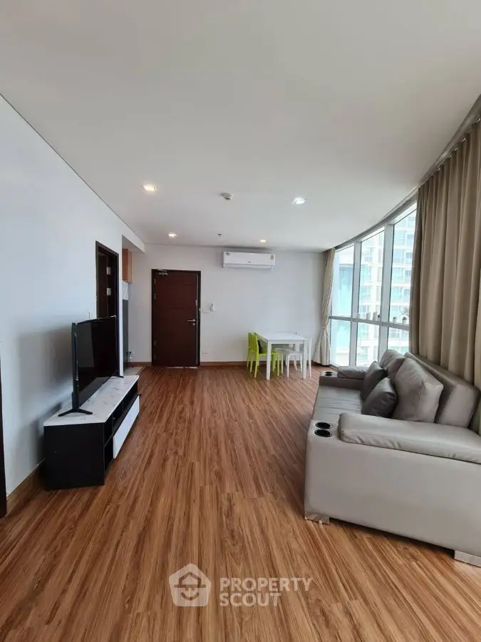 Spacious modern living room with wooden flooring and large windows in a high-rise apartment.