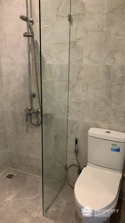 Elegant bathroom with marble tiles featuring a sleek glass shower enclosure and a modern Kohler toilet, perfect for contemporary living.