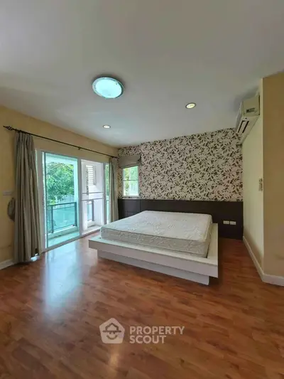 Spacious bedroom with large window and elegant wallpaper, featuring a comfortable bed and wooden flooring.
