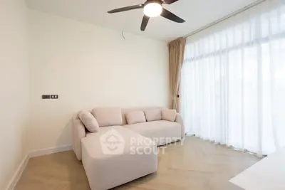 Modern living room with elegant beige sofa and ceiling fan, featuring large windows with sheer curtains.