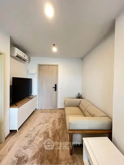 Modern living room with beige sofa, flat-screen TV, and wooden flooring in a cozy apartment.