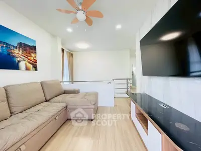 Modern living room with large TV and comfortable sofa, featuring elegant decor and ceiling fan.