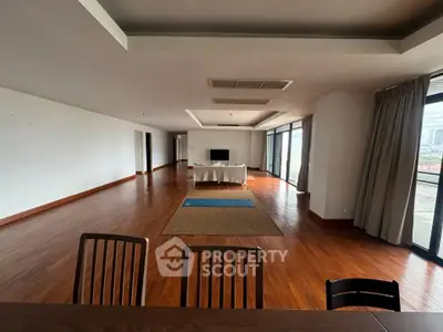 Spacious open-plan living room with wooden flooring and large windows offering city views.