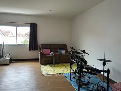 Spacious living room with drum set and cozy sofa, featuring large window for natural light.