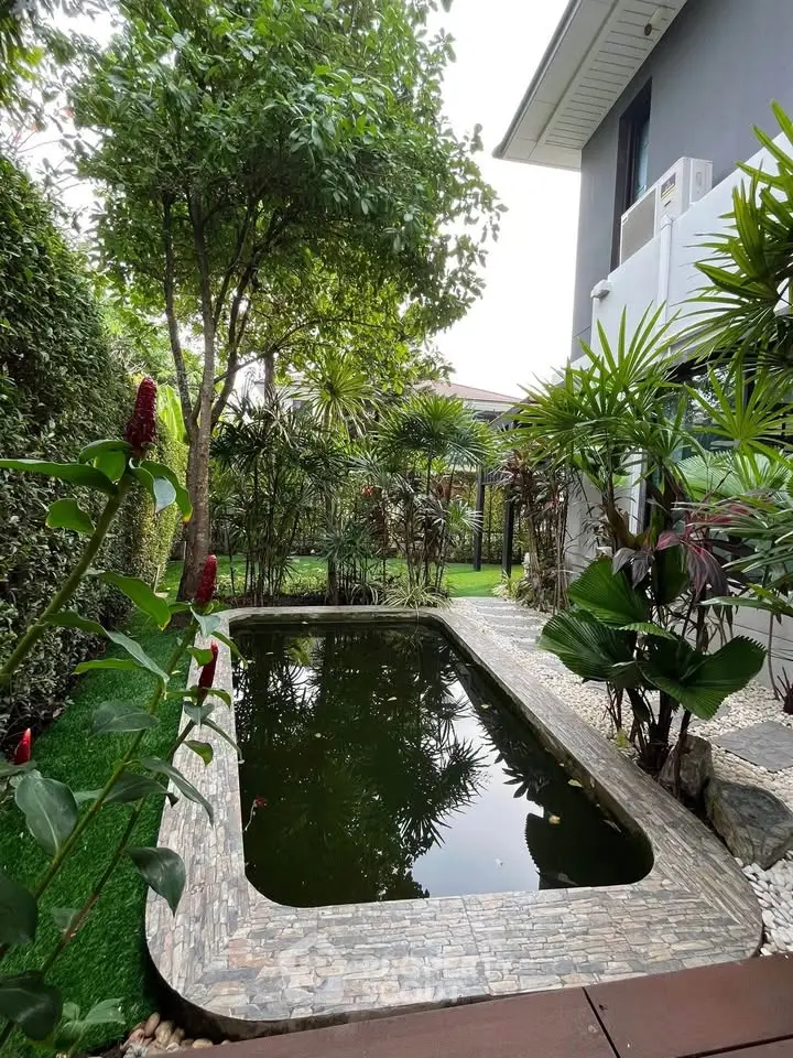 Charming garden with a serene pond and lush greenery beside a modern home exterior.