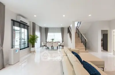 Spacious modern living room with elegant dining area and staircase, featuring sleek design and natural light.