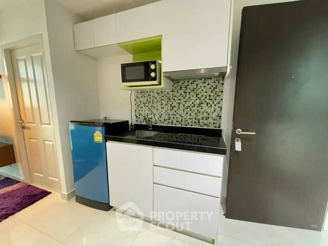 Modern compact kitchen with sleek cabinets, microwave, and mini fridge in stylish apartment.