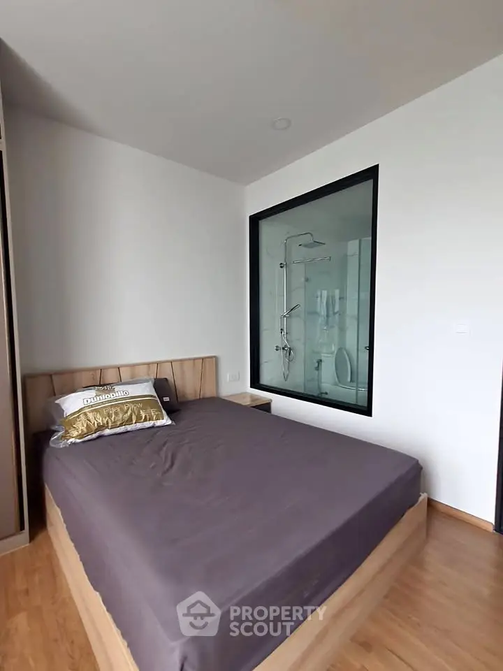 Modern bedroom with ensuite glass shower, wooden flooring, and minimalist design.