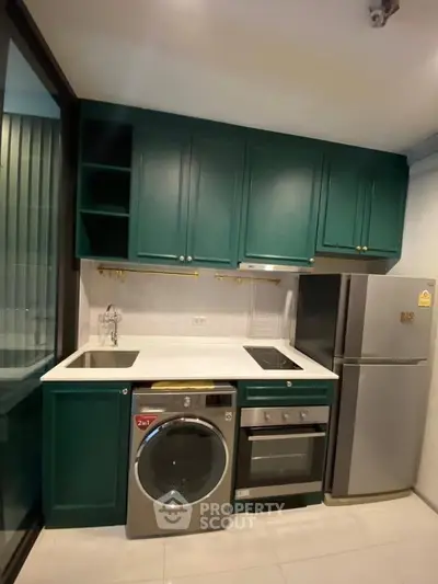 Modern kitchen with green cabinets, washing machine, oven, and fridge in compact layout.