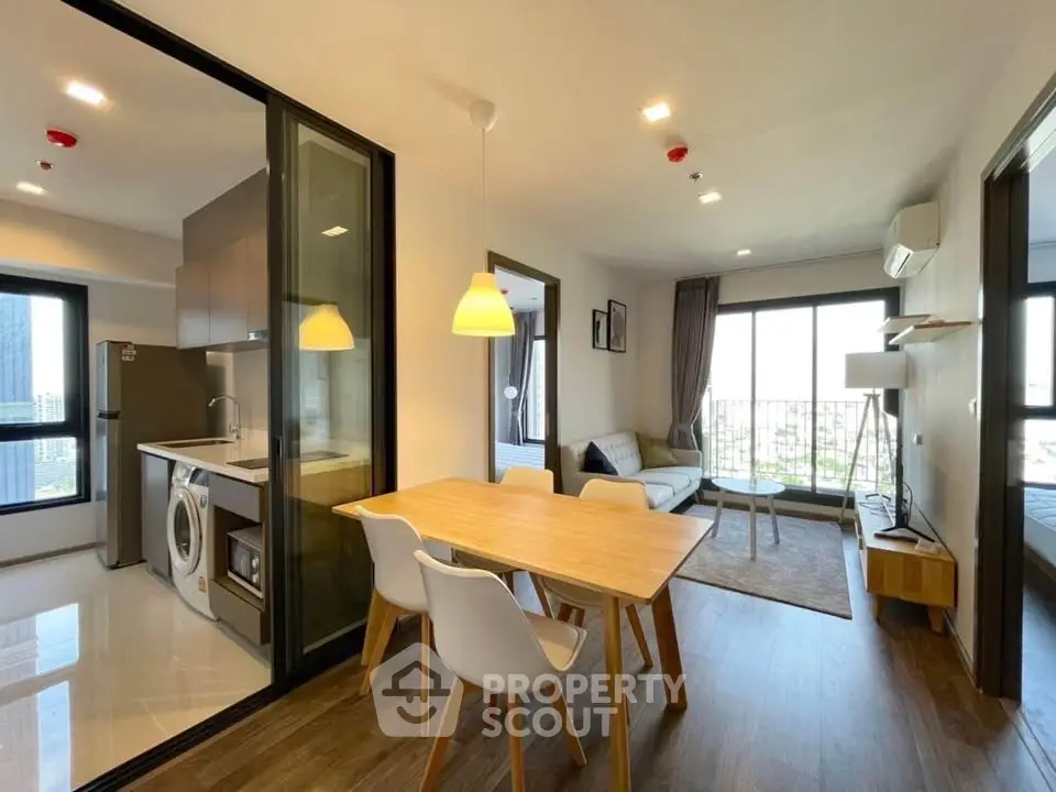 Modern open-plan living room with kitchen and dining area, featuring stylish furniture and large windows.