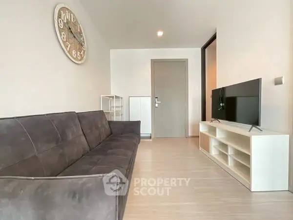 Modern living room with sleek sofa and wall-mounted TV, featuring minimalist decor and stylish clock.