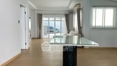 Spacious modern living room with glass table and large windows offering natural light.