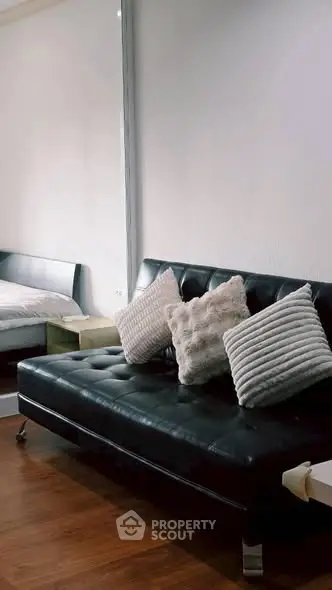 Modern living room with stylish black leather sofa and cozy cushions, featuring sleek wooden flooring.