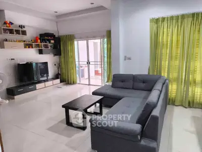 Spacious living room with modern gray sofa and entertainment center, featuring large windows and green curtains.
