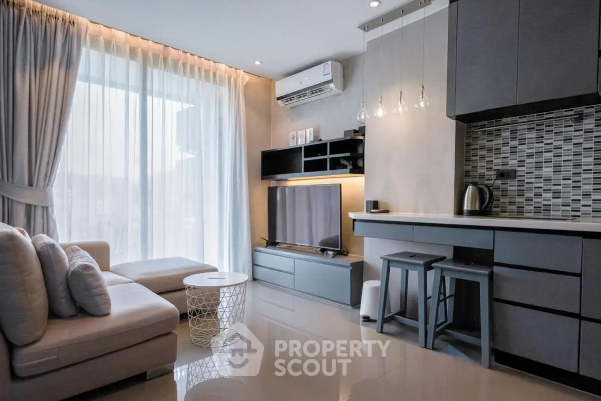 Modern living room with sleek furniture and stylish kitchen area, featuring natural light and contemporary design.