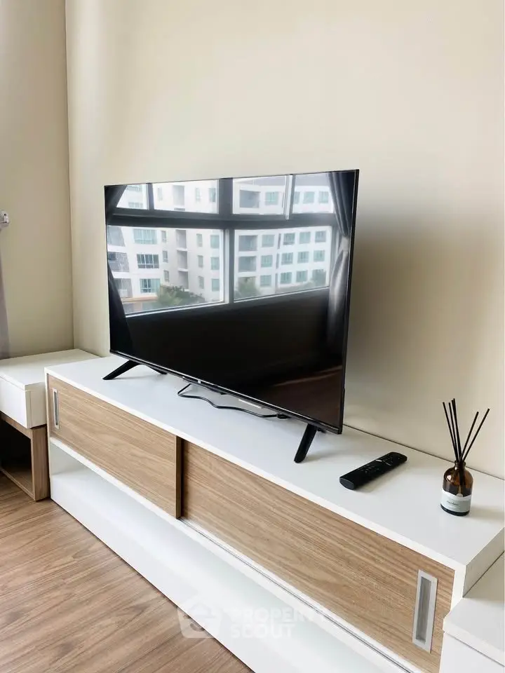 Modern living room with sleek TV on stylish wooden cabinet, large window view reflecting urban landscape.