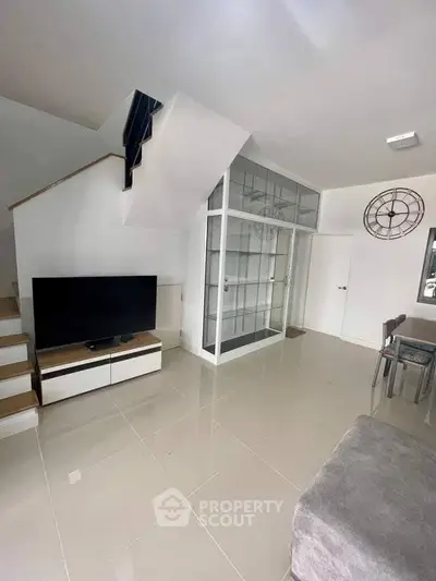 Modern living room with sleek staircase and glass partition, featuring a large TV and stylish decor.