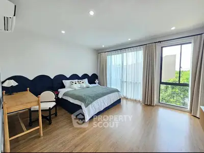 Spacious bedroom with modern decor and large window offering natural light and greenery view.