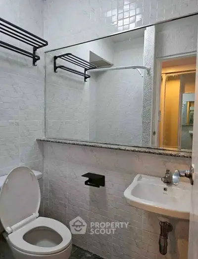 Compact bathroom with white tiles, wall-mounted sink, and toilet in modern apartment.