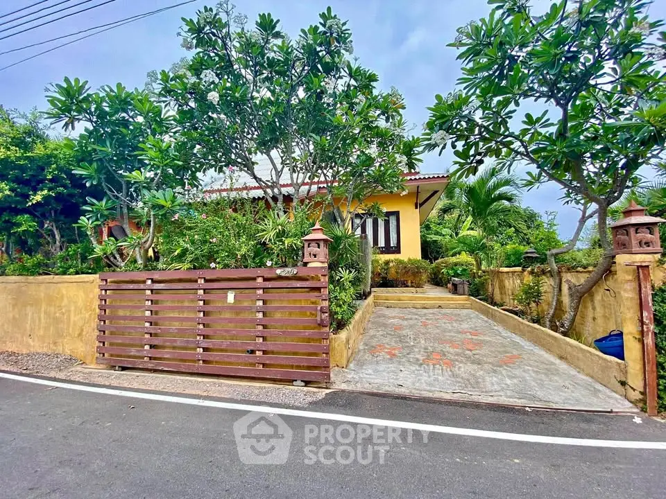 Charming yellow house with lush garden and gated driveway in serene neighborhood.