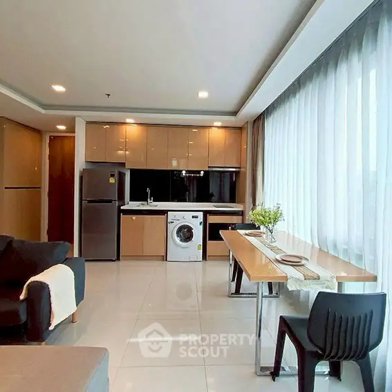 Modern open-layout living room with kitchen, featuring large windows and sleek furniture.
