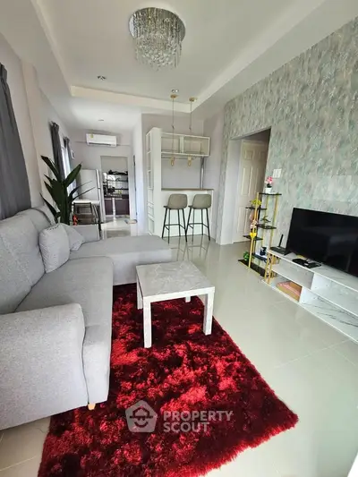 Stylish living room with modern decor, featuring a plush red rug, grey sectional sofa, and chic lighting.