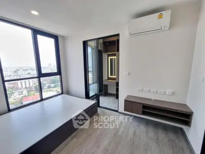 Modern bedroom with large windows offering an expansive city view, sleek flooring, and a cozy nook, perfect for urban living.